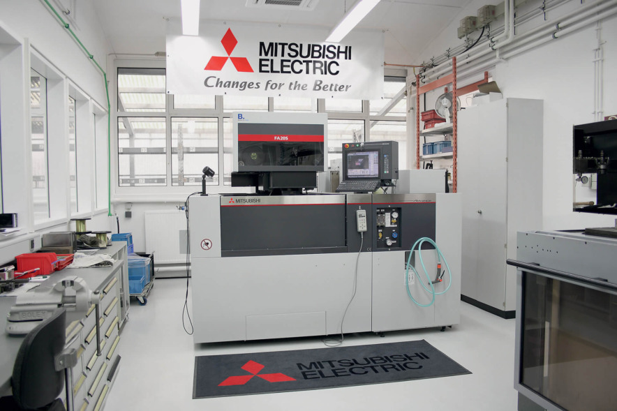 Mit dem Werbebanner von Mitsubishi Electric über der Maschine und dem großen Teppich davor ähnelt der Raum einer Kultstätte.