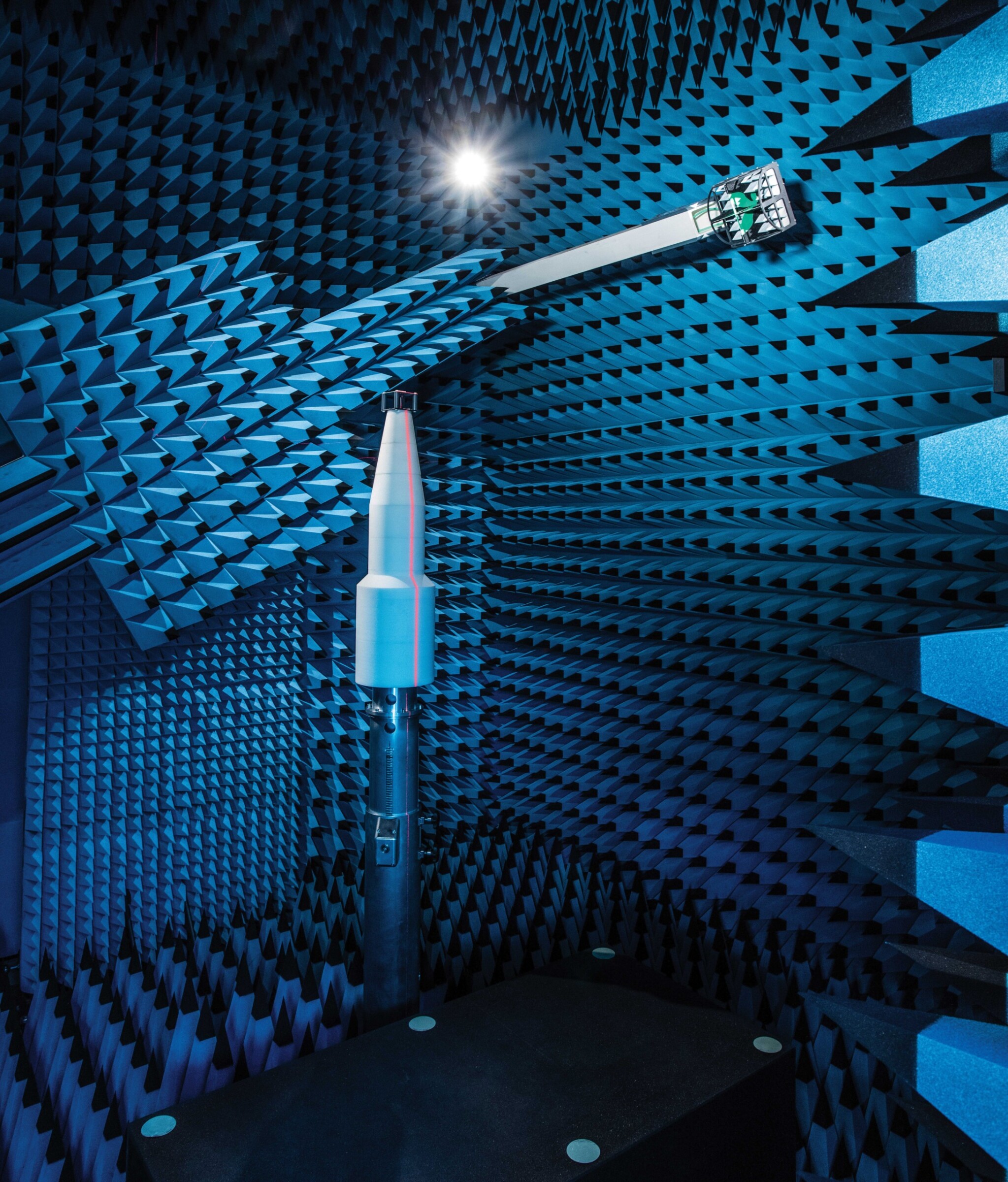 At Rohde & Schwarz, both large, wide-reach and small antennas are measured and tested in chambers such as these. The picture shows a small black specimen on a conical, white support.
