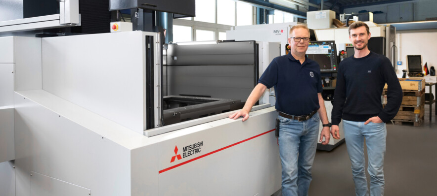 Stefan Menke (links) und Dominic Janoschka (rechts) vor der neuesten Erwerbung – der Mitsubishi Electric Drahterodiermaschine MV4800S NewGen.